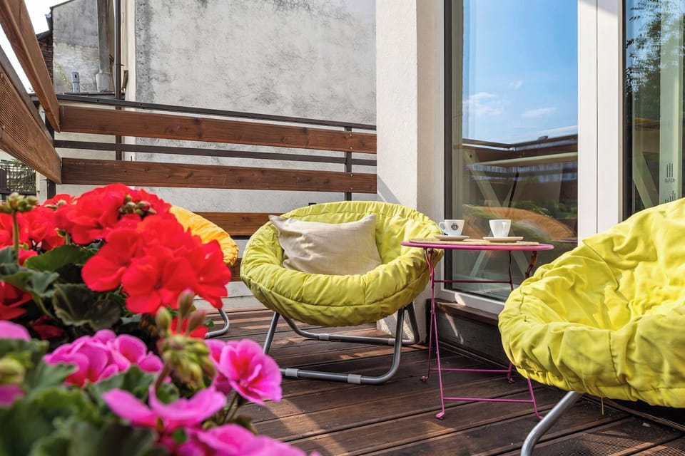 A closer outdoor view highlights yellow seating surrounded by red flowers and greenery. The terrace creates a cheerful resting area.