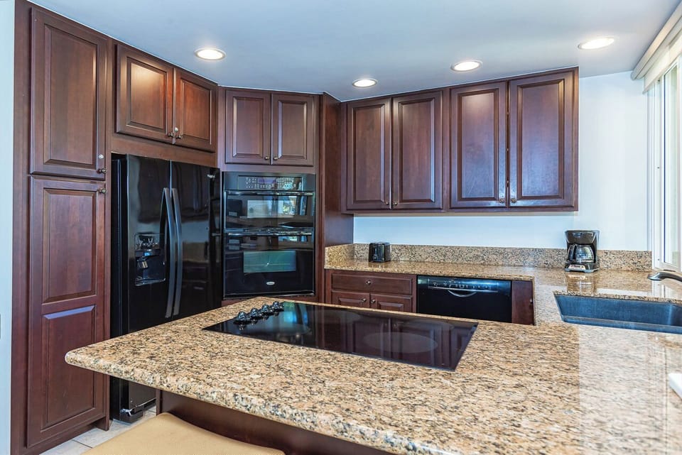 Your gourmet kitchen awaits with gleaming granite countertops, rich wood cabinetry, perfect for preparing meals by the window.