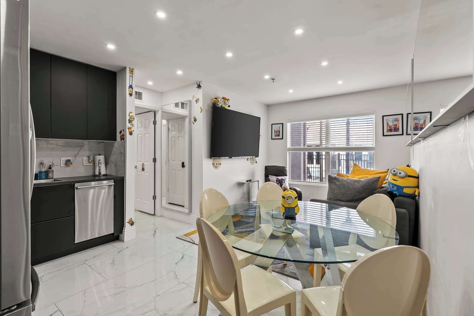 Open-plan living & dining area w/ a glass table, modern chairs, & a sleek mounted TV.
