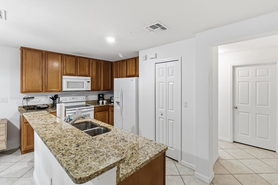 Granite countertop wraps around the kitchen island with a double sink, oak cabinets, and white appliances.