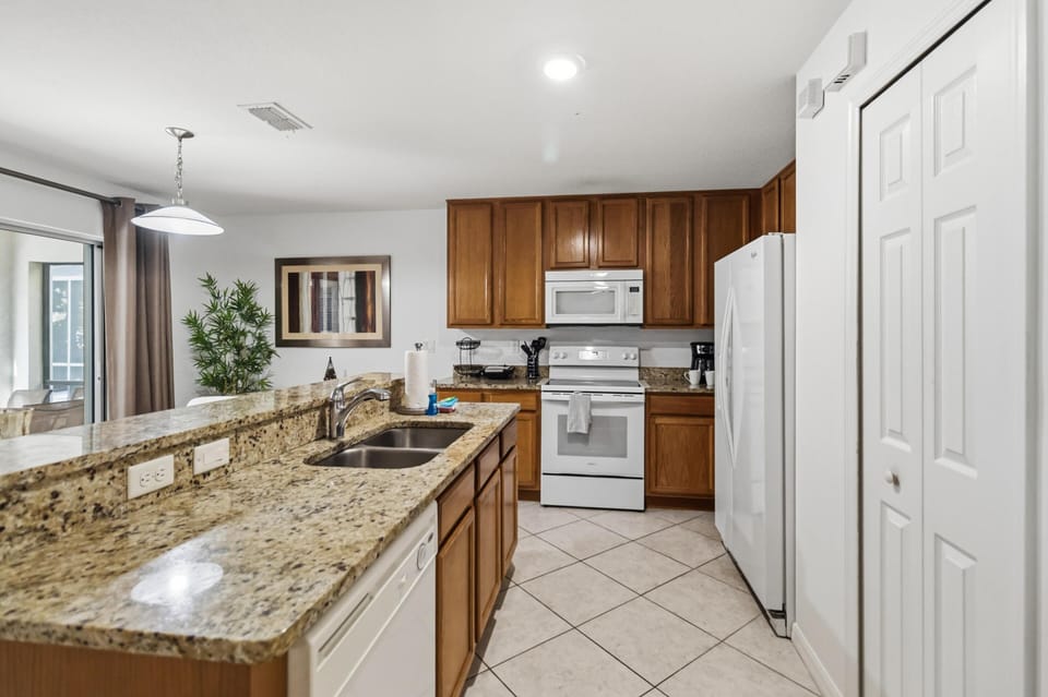 Granite countertops with double sink extend into breakfast bar, facing oak cabinetry and white appliances.
