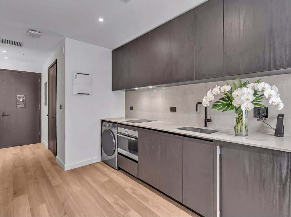 Sleek modern kitchen with rich dark cabinetry, full-size washer/dryer, oven, and stainless sink. Under-cabinet lighting and warm wood floors add style and warmth. Fully equipped and beautifully finished for easy, comfortable living.