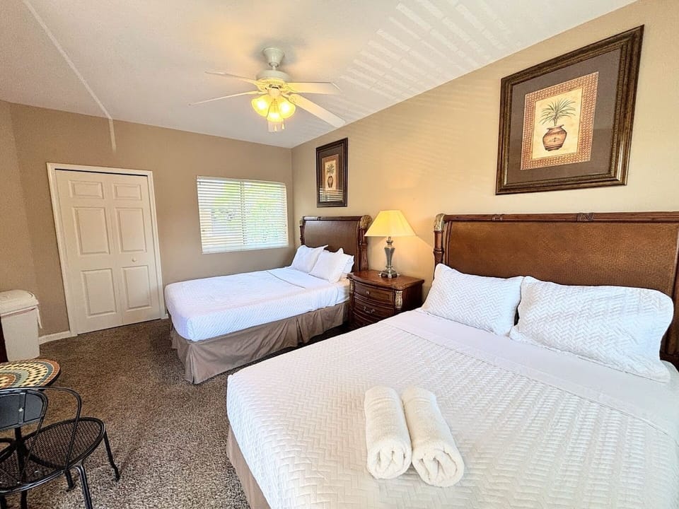 Spacious bedroom with two beds, ceiling fan, bedside lighting, and a clean, relaxing layout.