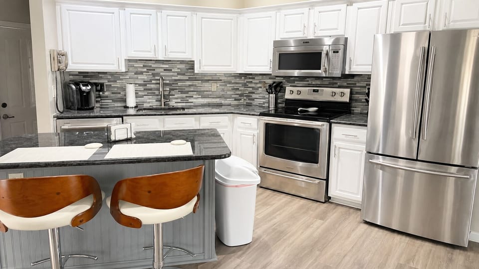 Modern kitchen with white cabinetry, stainless steel appliances, tile backsplash, breakfast bar seating, and wood-look flooring.