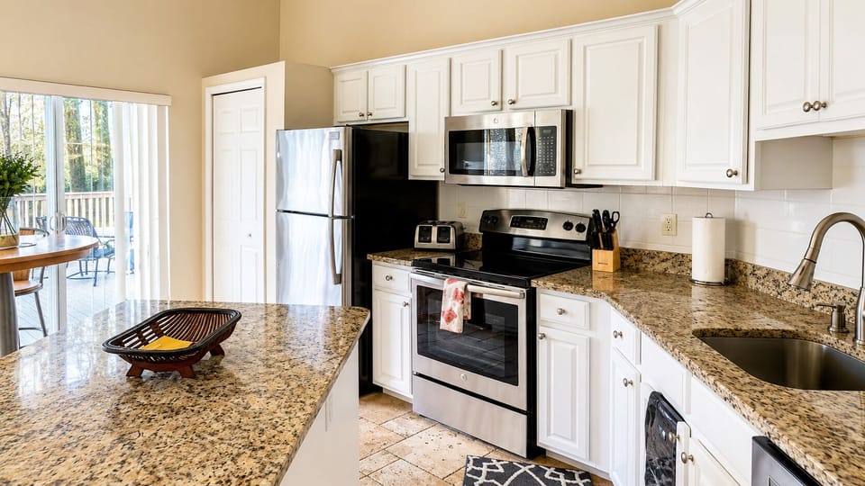 Updated kitchen with granite countertops, stainless steel appliances, white cabinetry, and convenient counter space.