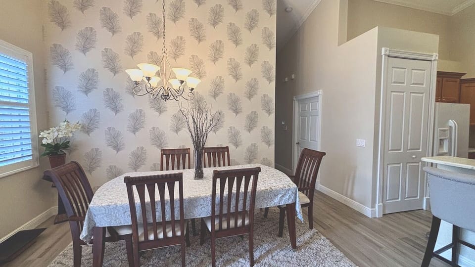 Share memorable meals under the warm glow of a classic chandelier, accented by stylish, contemporary wallpaper that adds a touch of sophisticated flair.