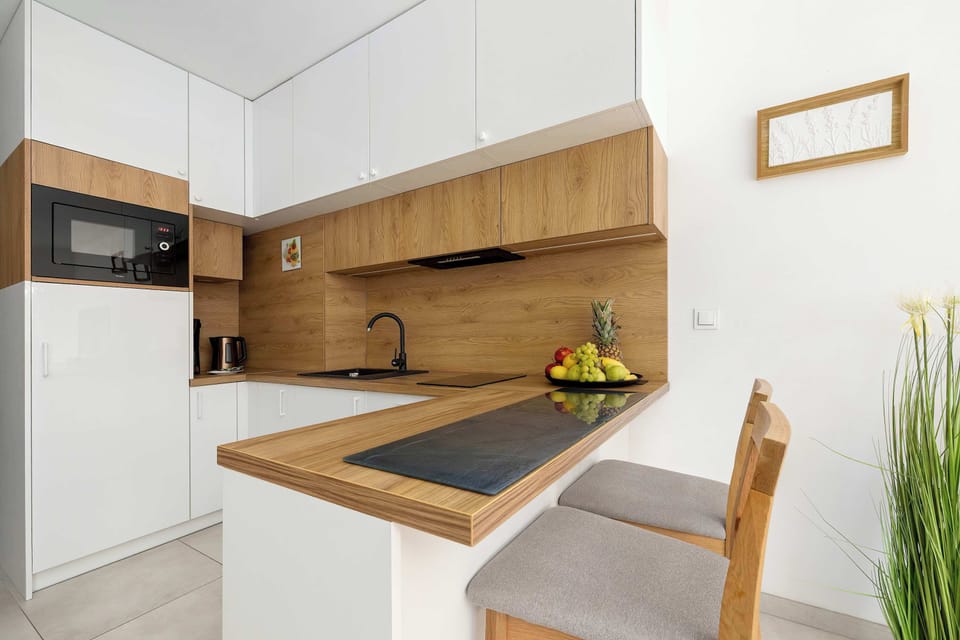 A modern kitchenette with white cabinets and wooden countertops. The space is bright and neatly arranged.
