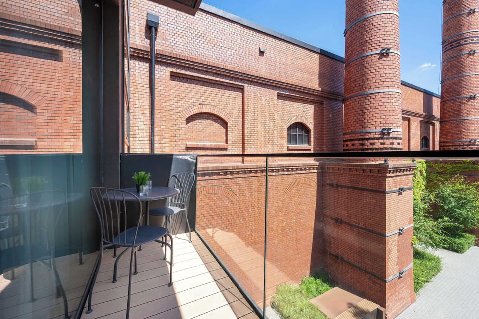 A second balcony view emphasizes the red-brick industrial-style structures surrounding the property. Glass railings preserve the open outlook.