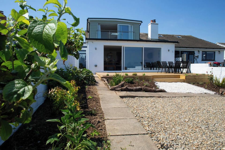 Modern white house with patio doors and outdoor dining set, viewed from the garden path