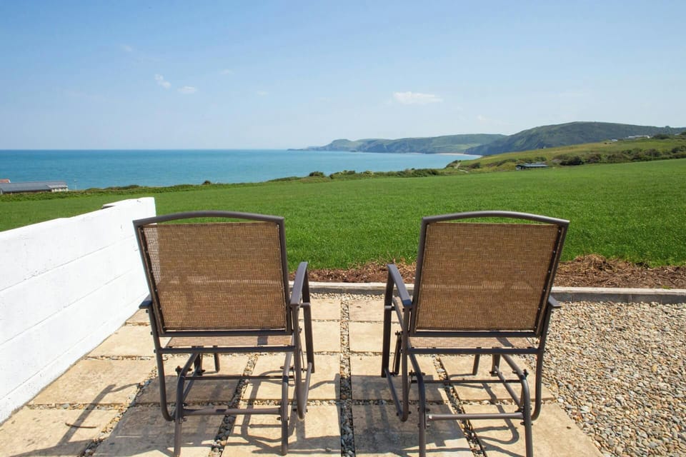 Two patio chairs facing a grassy field and sea view