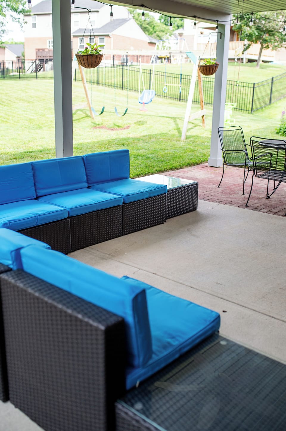 Covered patio with lounge seating, fenced yard, and family-friendly swing set