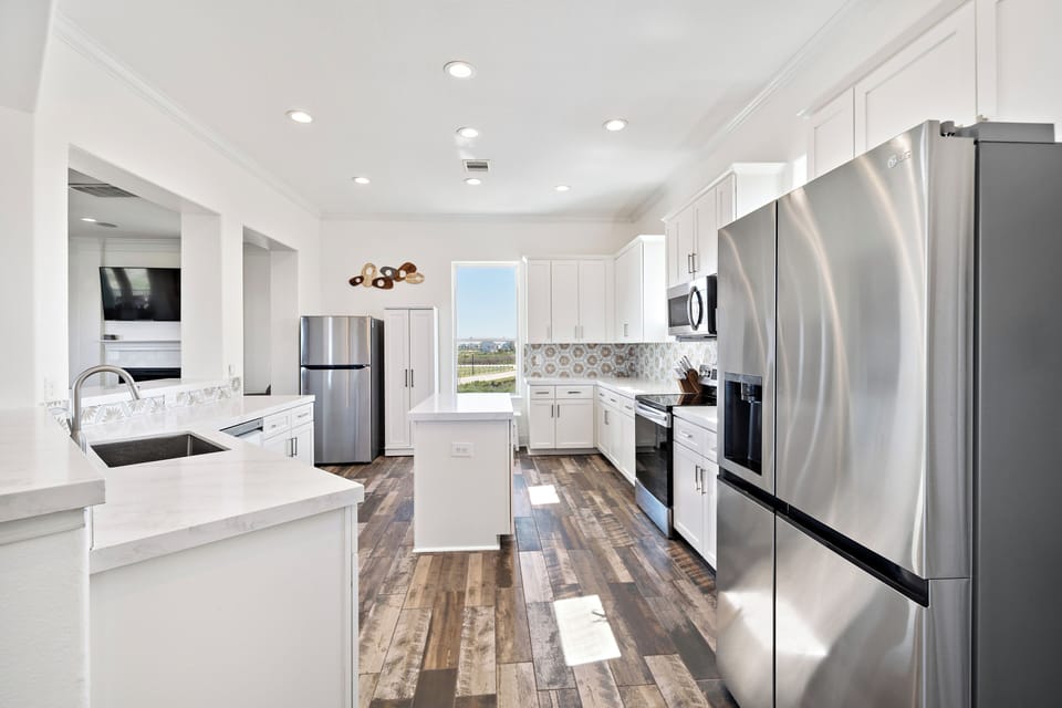 Modern kitchen with stainless steel refrigerator, white cabinetry, spacious counters, and bright lighting. Fully equipped space for preparing family meals.