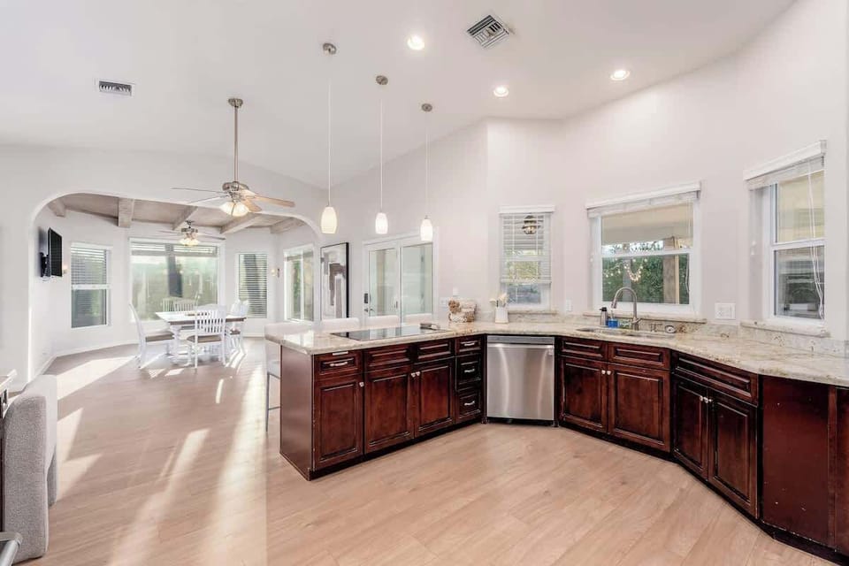 Sunlight fills your open-concept living space, where rich wood cabinetry and granite countertops meet soaring ceilings. Step from kitchen to dining with ease as natural light streams through every window.