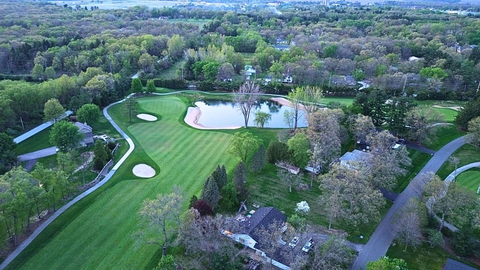 “Stunning aerial view featuring lush fairways, sand traps, and a scenic pond—golf at its finest.”
