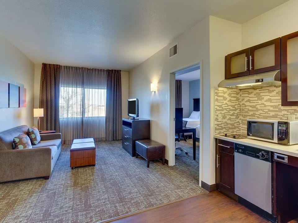 Living space with sofa, coffee table, wall-mounted flat-screen TV, and kitchen with dishwasher, microwave, and dark wood cabinetry.