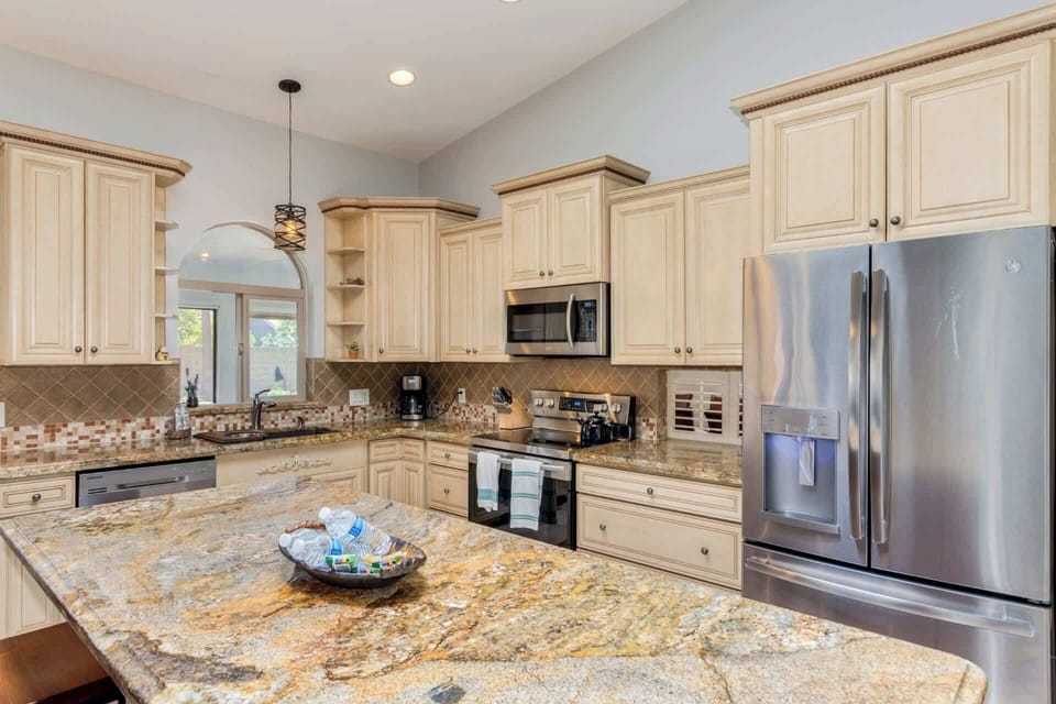 Open concept kitchen with stainless steel appliances, granite countertops, kitchen island with breakfast bar seating for 3, and coffee maker 