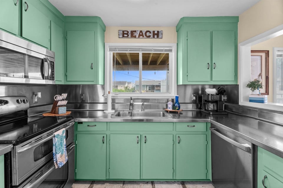 Bright kitchen with stainless steel appliances, double sink, generous counter space, and natural light from the window overlooking the outdoor deck.
