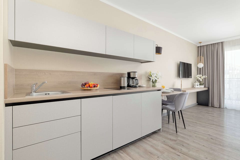 A wide-angle view of the long kitchenette unit integrated into the living space. The minimalist design features seamless handleless cabinets and a small workspace at the far end.