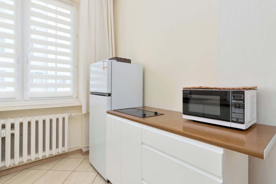 A compact kitchen with white cabinets and wooden countertops. A microwave and refrigerator provide practical amenities.