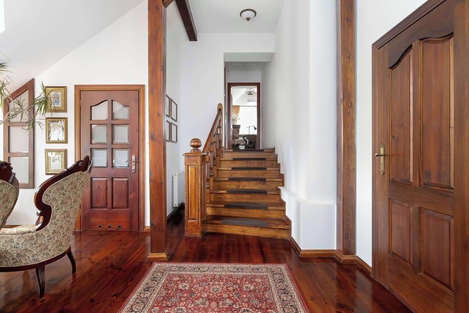 A hallway perspective leading toward a staircase, with wooden doors and a patterned rug adding warmth to the interior.