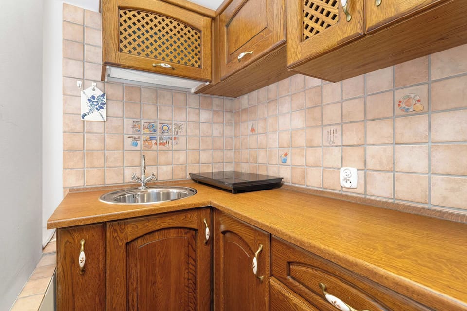 A rustic kitchen with wooden cabinetry, tiled walls, and a compact cooking area. Warm wood tones dominate the space.