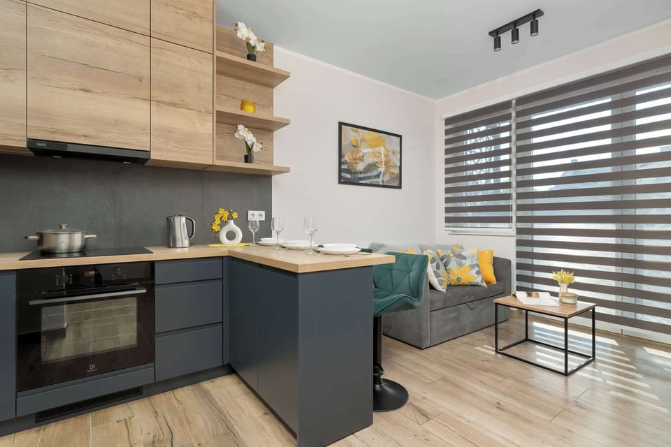 A bright open-plan living area connected to a modern kitchenette. Large windows bring in natural light, creating a welcoming atmosphere.