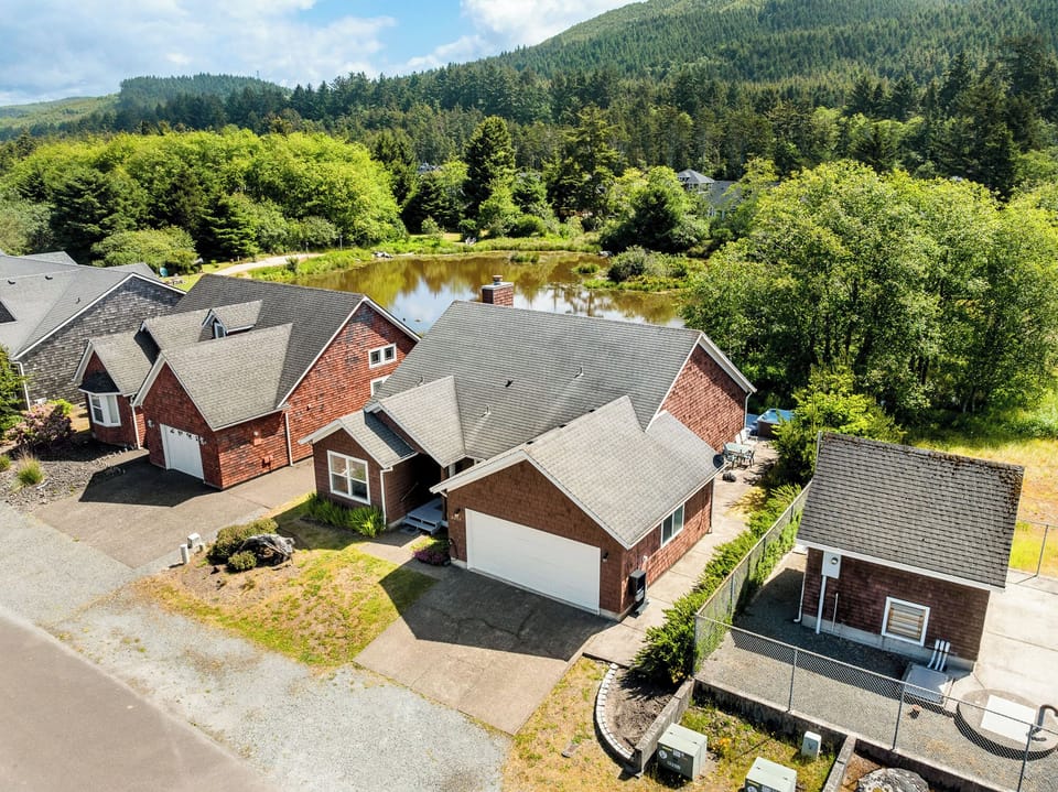 Aerial view of residential properties nestled beside a tranquil pond, surrounded by lush forests and mountains, showcasing the peaceful natural setting of the vacation rental area.