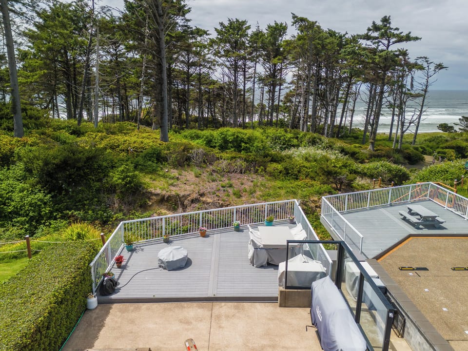 Seaside decks offer multiple gathering spaces with ocean views through coastal trees, perfect for morning coffee or evening sunsets in the surrounding natural landscape.