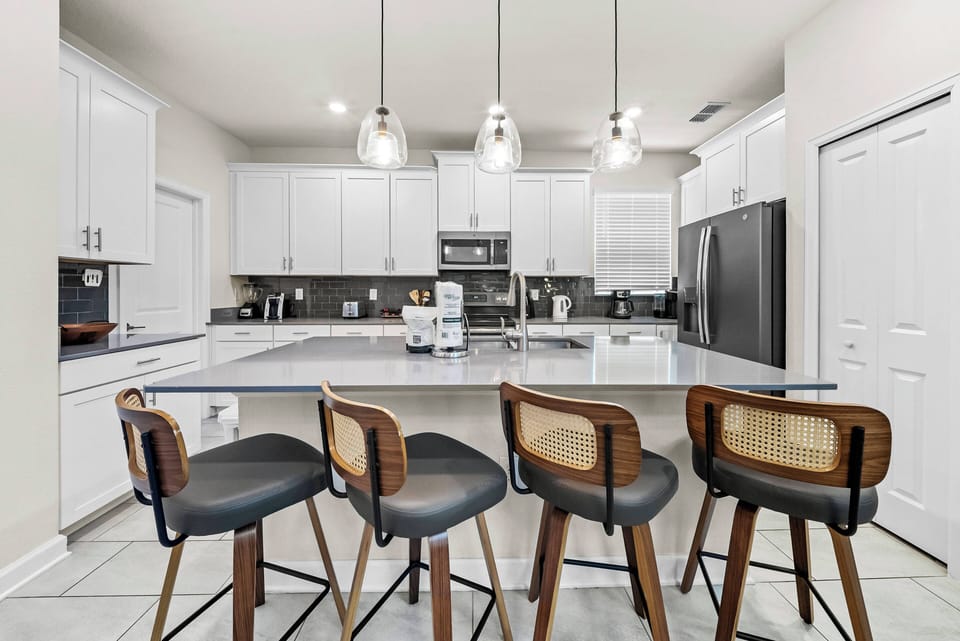 This stylish kitchen boasts a spacious island with trendy bar stools, ideal for casual meals or morning coffee. The bright white cabinetry and contemporary lighting create a welcoming space for your culinary adventures.