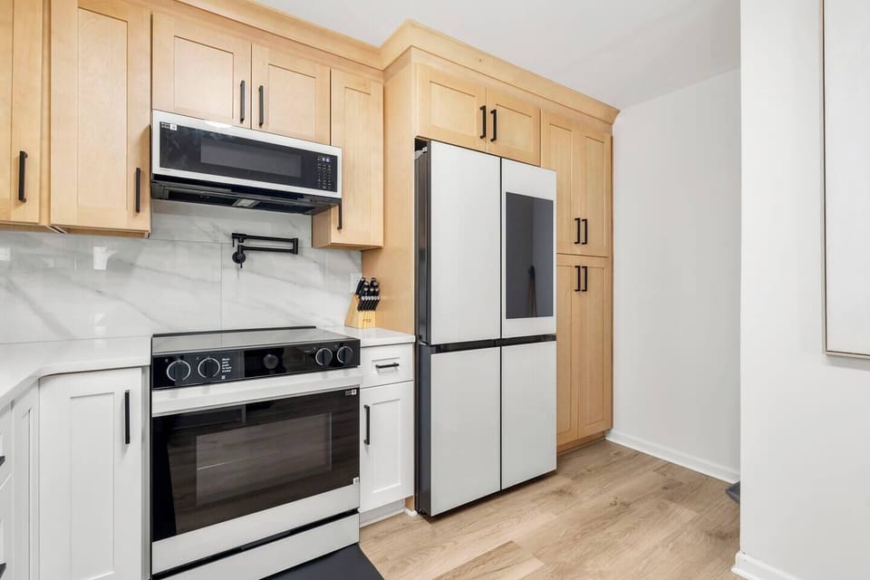Equipped with a sleek glass cooktop, pot filler, and smart Samsung appliances, this kitchen combines high-performance features with timeless cabinetry and modern finishes. Designed for convenience and crafted for style.