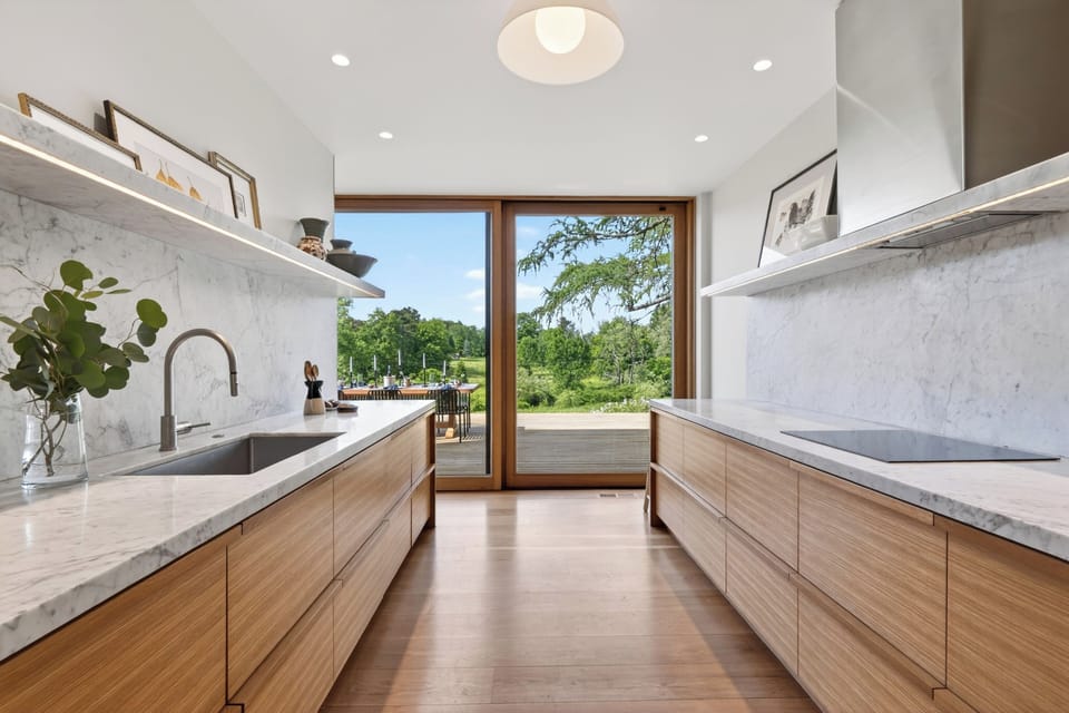This sleek, dual-island kitchen layout boasts a minimalist design and a massive sliding glass door leading to the outdoor terrace.