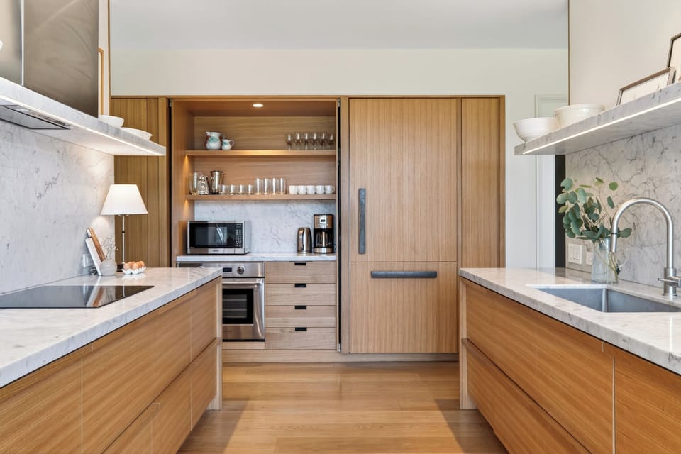 A chef’s kitchen featuring warm, custom flat-panel oak cabinetry, clean countertops, and smart built-in appliance integration.