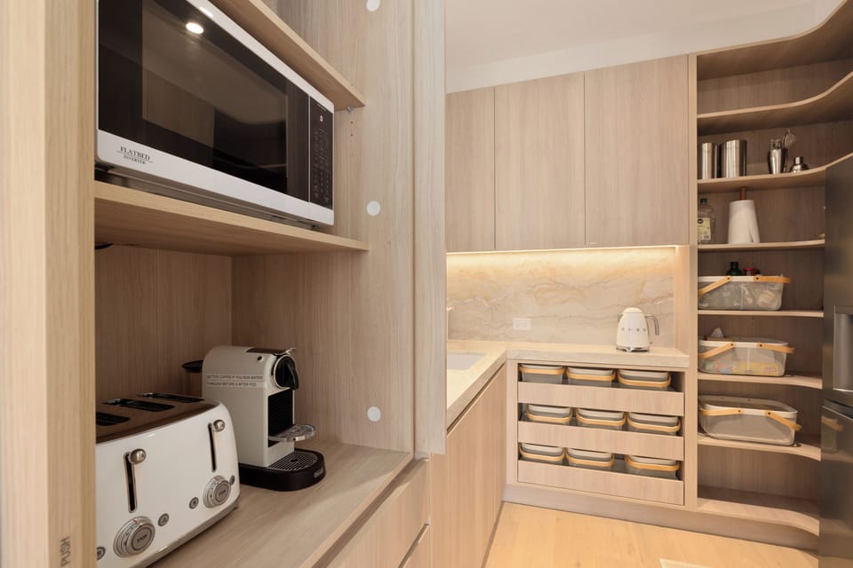 Sleek kitchen with espresso maker, toaster, organised pantry and warm lighting.