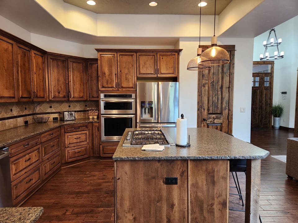 Your culinary haven awaits with rich wood cabinetry, granite counters, and top-tier appliances. The spacious island invites meal prep and gathering, while pendant lighting adds warmth to every moment you create here.