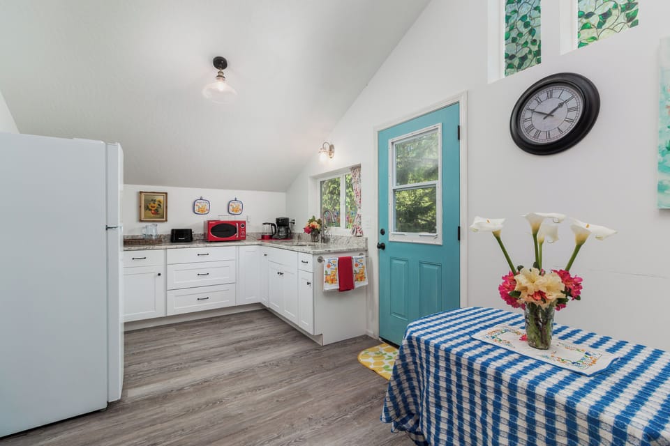 Your charming kitchen awaits with bright white cabinets, granite counters, and a cheerful turquoise door framing garden views—perfect for morning coffee or prepping meals together.
