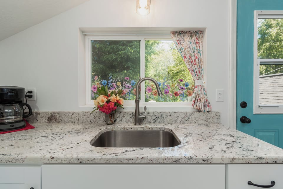 Imagine preparing meals at this charming kitchen sink, where sunlight streams through the window framing a vibrant garden view. Fresh flowers and bright touches invite you to feel right at home.