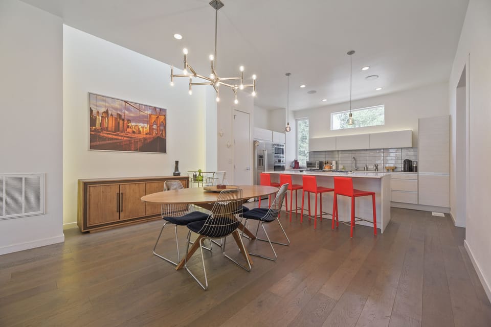 Gather with loved ones in this airy, sunlit space where your morning coffee meets modern elegance—sleek countertops, bold red bar stools, and a dining area that invites laughter and long conversations.
