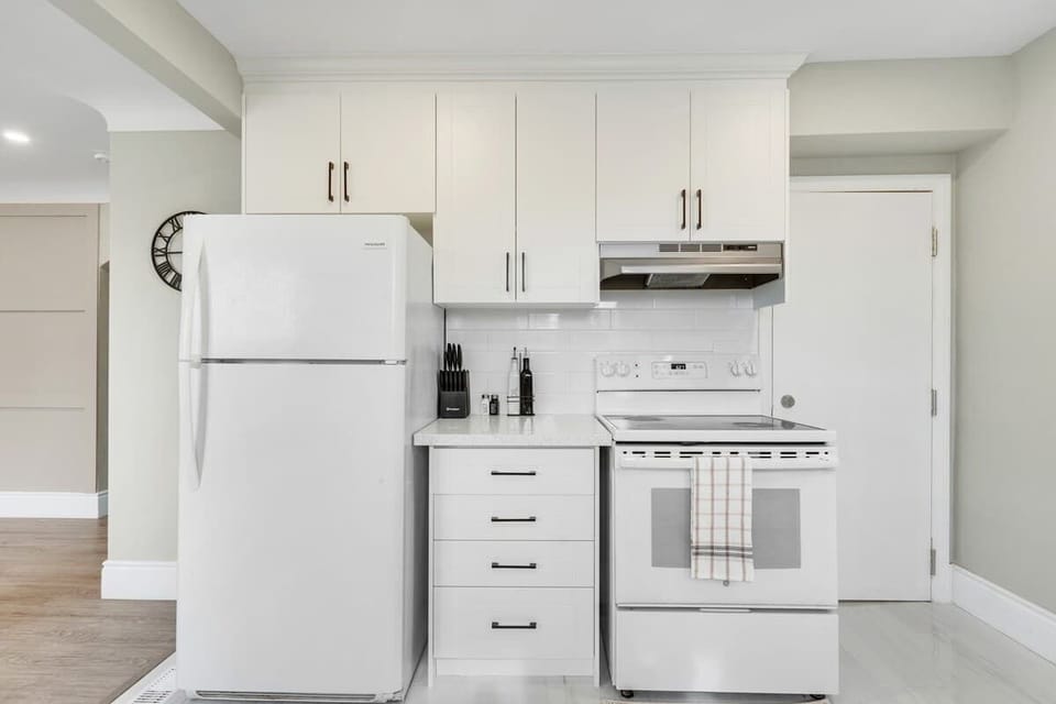 Cozy kitchen with spacious refrigerator, electric stove with hood, sleek cabinetry, knife set, cutting board, and convenient countertop space.