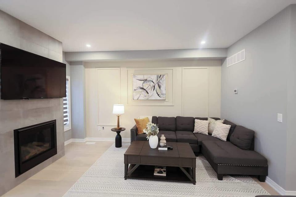 Stylish living space with a cozy sectional sofa, chic throw pillows, sleek fireplace, large smart TV, elegant coffee table, modern lamp, and wall art.