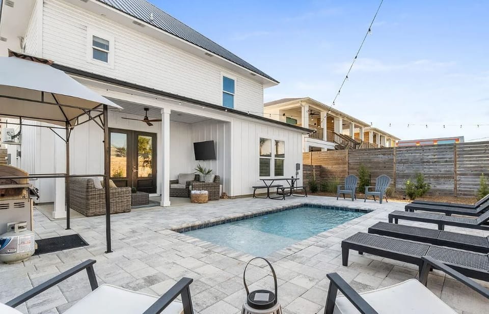 A beautifully designed outdoor oasis featuring a sparkling pool, comfortable lounge chairs, covered patio seating, and modern privacy fencing—perfect for relaxing under sunny skies.