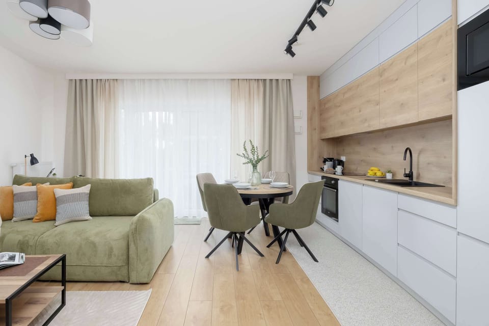 The layout transition highlights the smooth connection between the cozy lounge and the sleek, handle-less kitchen. The light-colored flooring helps to maximize the open feel of the entire room.