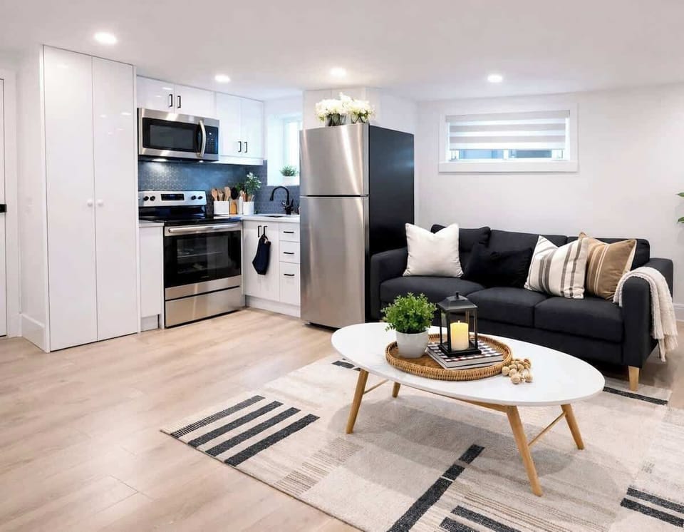 Bright, modern open-concept living space featuring a fully equipped kitchen, stainless steel appliances, cozy sofa seating — thoughtfully designed for comfort and extended stays.