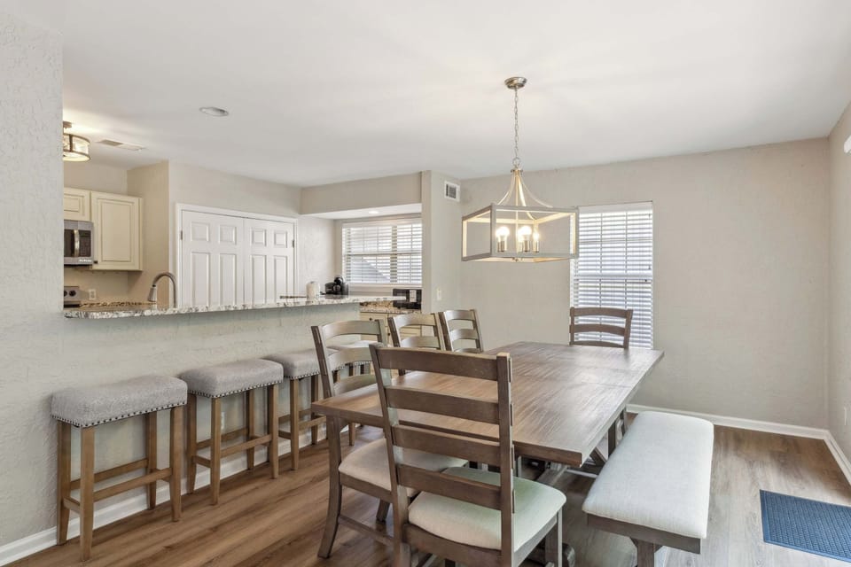 Granite counters and a sturdy wooden dining table anchor this open heart of the home, where soft afternoon glow meets crisp, neutral tones. Padded seating and a modern lantern fixture invite slow mornings and shared meals in a clean, calm space.