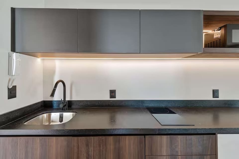 Sleek kitchenette close-up with modern induction cooktop, deep sink, and premium matte black hardware. Cabinets stocked with essential cookware for easy meals.