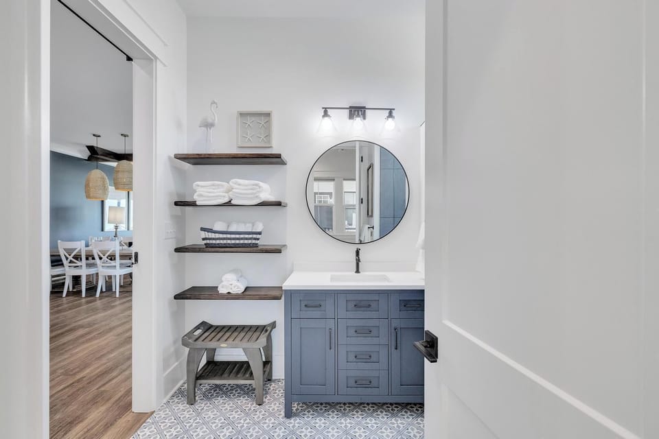 Refresh in your stylish bathroom, where coastal-inspired blue cabinetry, warm wood shelving stocked with fresh towels, and modern fixtures create a serene retreat after a day of adventure.