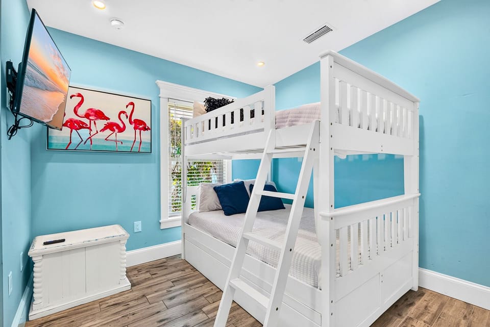 Bright coastal bunk room with TV, shutters, and fun flamingo decor