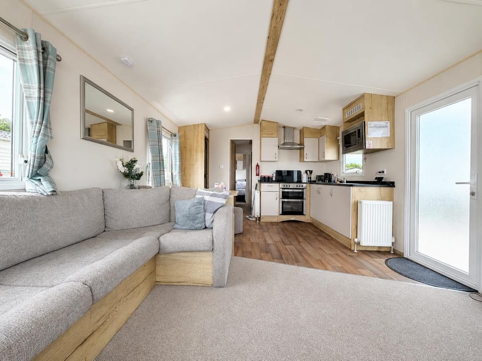 Open-plan living area featuring a beige fabric corner sofa, wood-effect kitchen cabinets, and vinyl plank flooring.