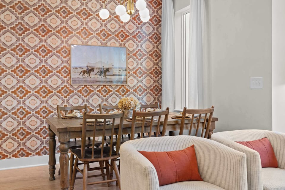 Dining area with farm table seating six, bold accent wall, western-inspired artwork, and gold chandelier. 