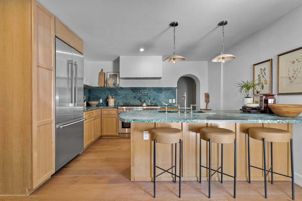 Chef's kitchen from the dining side — stainless refrigerator, green marble island, and pendant lights