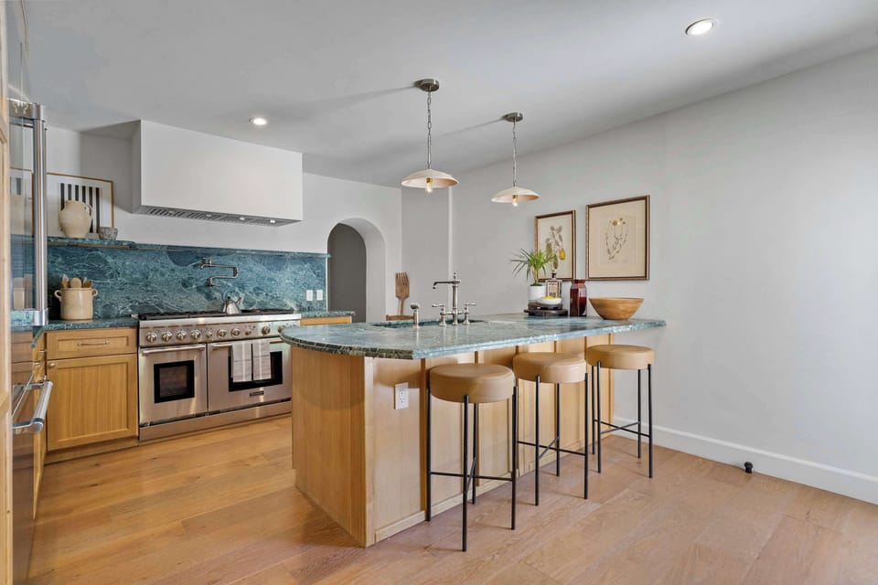 Chef's kitchen island with green marble countertop, pro-grade range, leather bar stools, and arched hallway